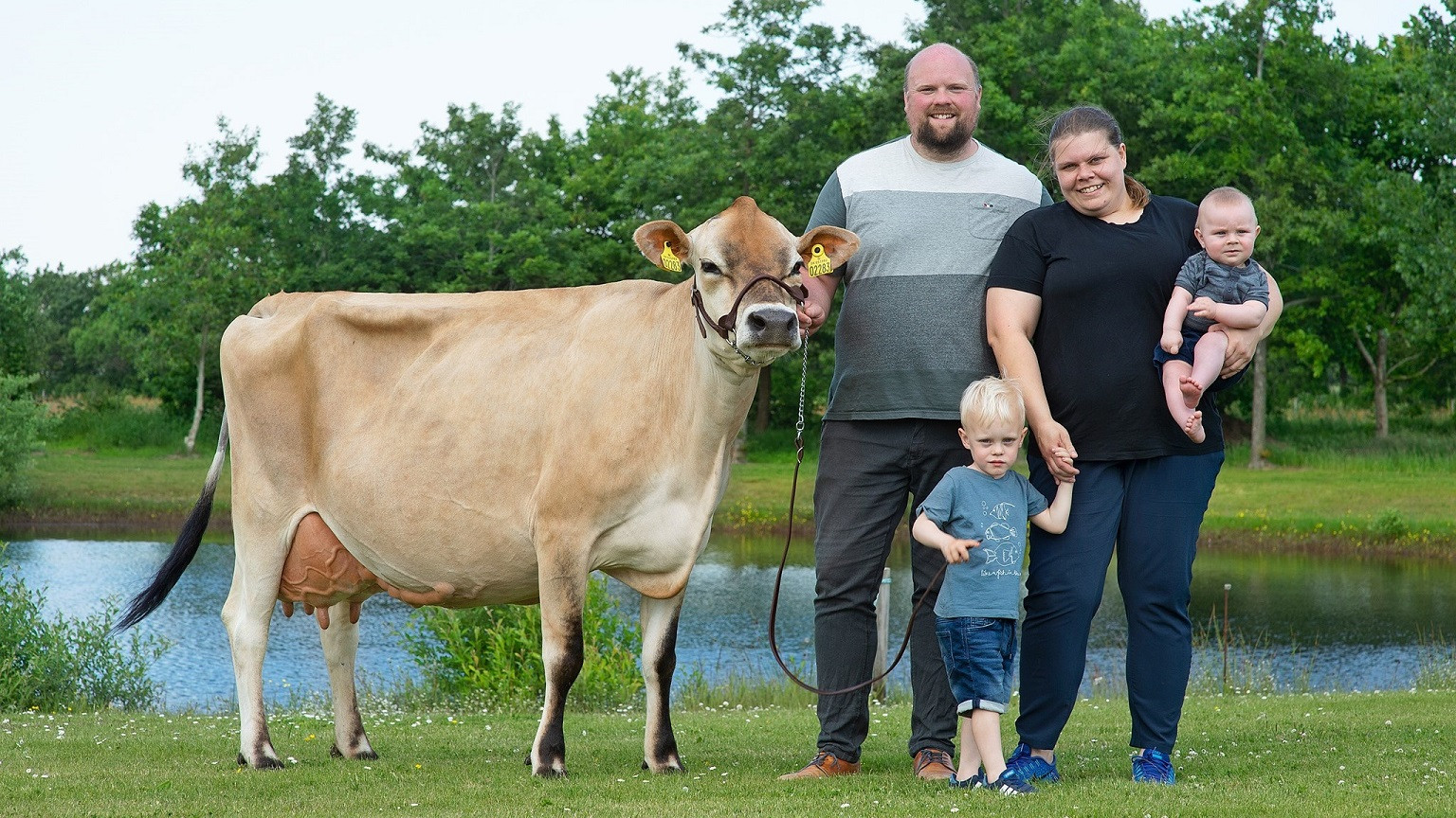 Jens og Tanja Rasmussen står med deres to børn og en ko ved en sø
